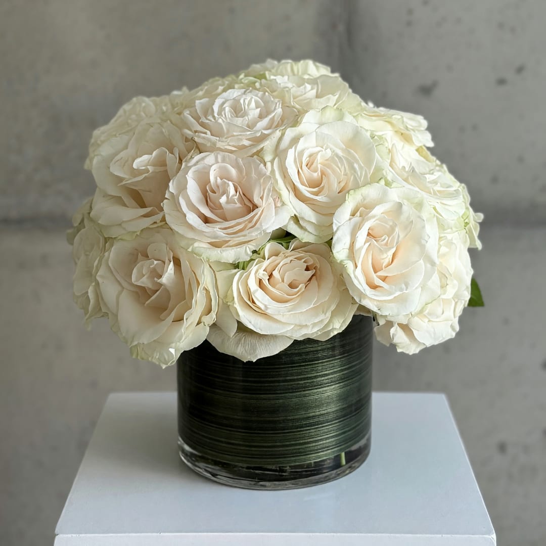White roses arranged in a dark glass vase on a white pedestal