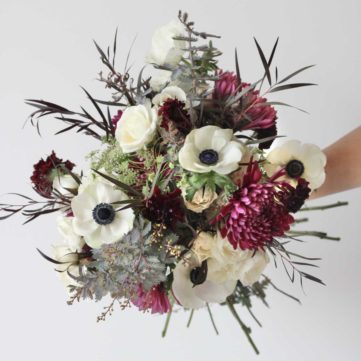 Bouquet of white anemones and magenta blooms with dark foliage