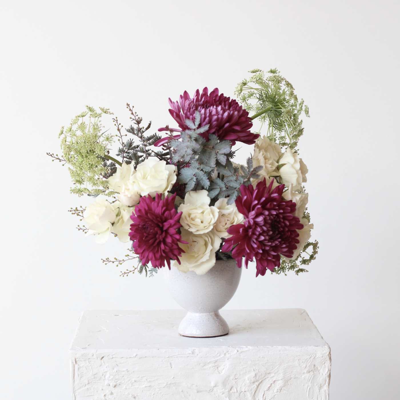 Magenta and white flowers arranged in a white pedestal vase
