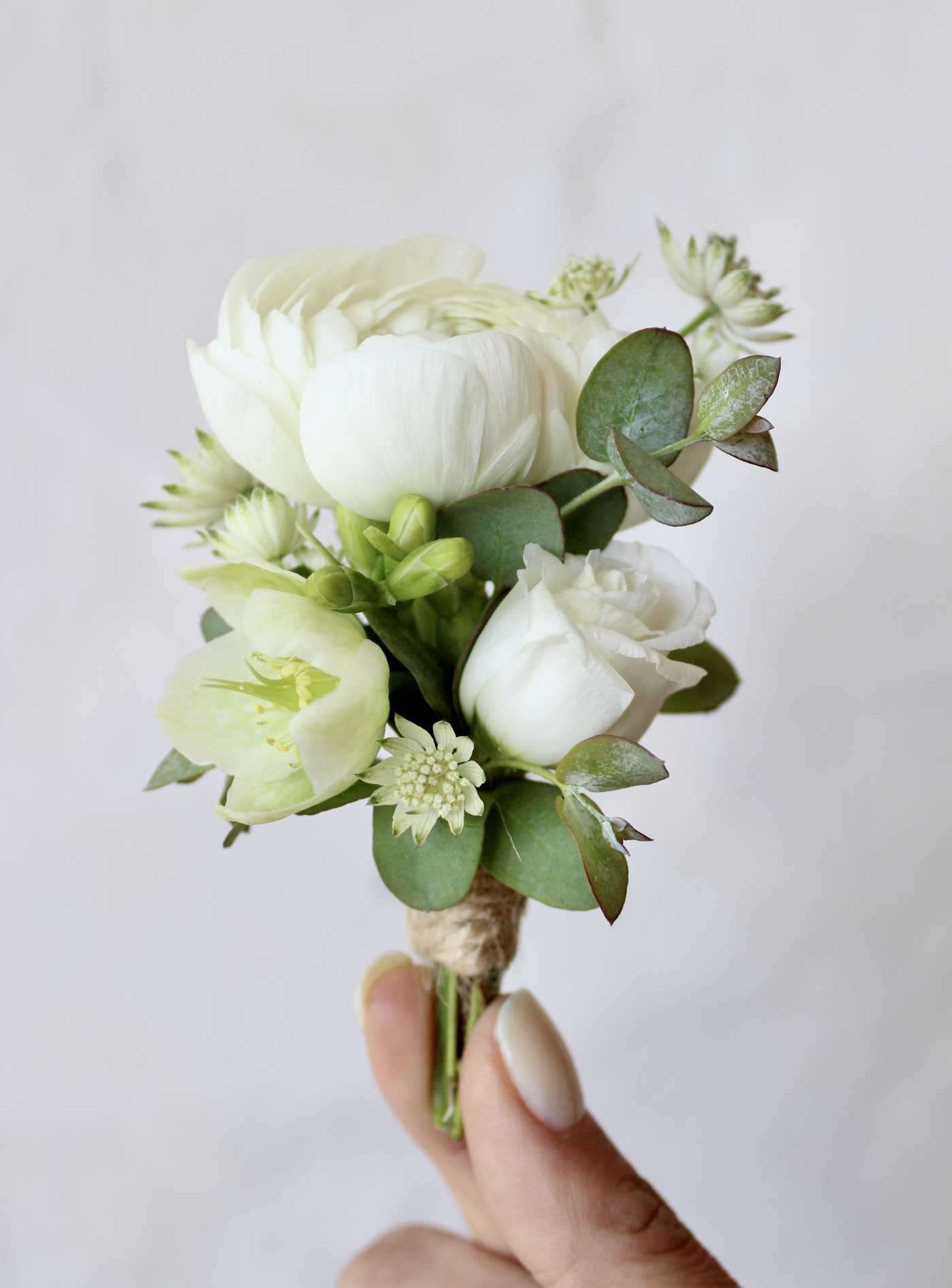 Small white floral boutonniere with green foliage held in a hand