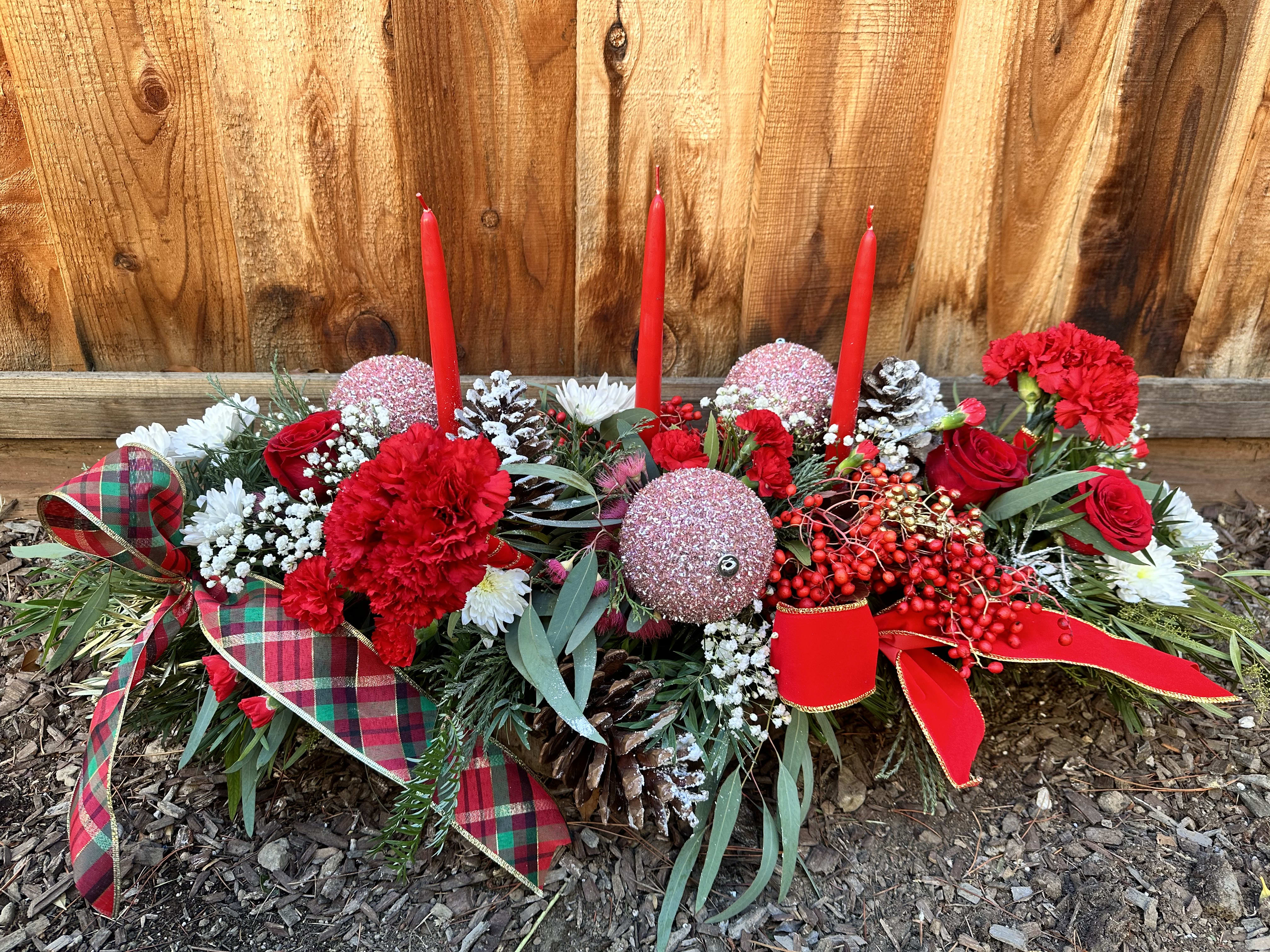 Holiday floral centerpiece with red candles, red flowers, and plaid ribbon