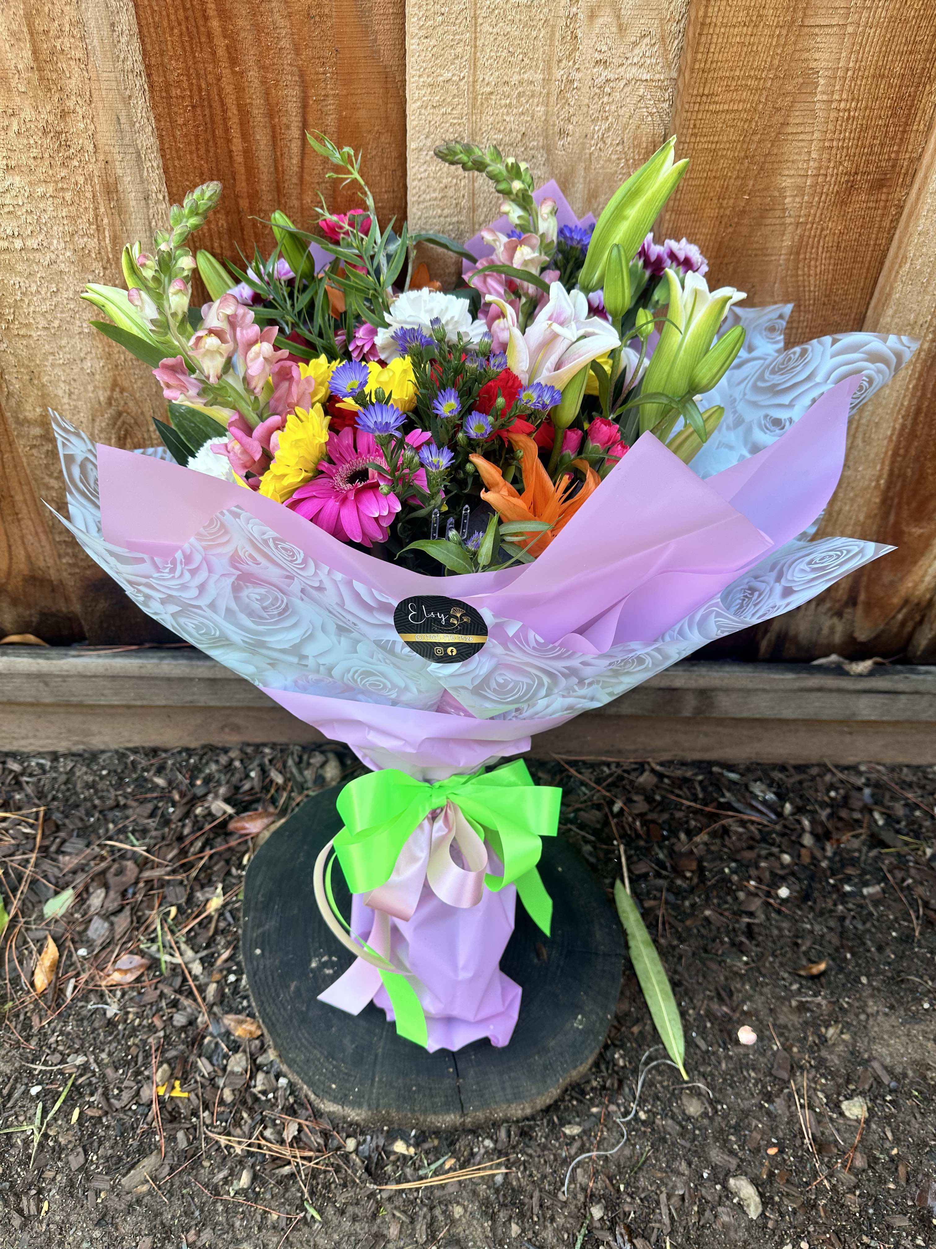 Mixed bouquet of colorful flowers wrapped in pink paper with a green ribbon