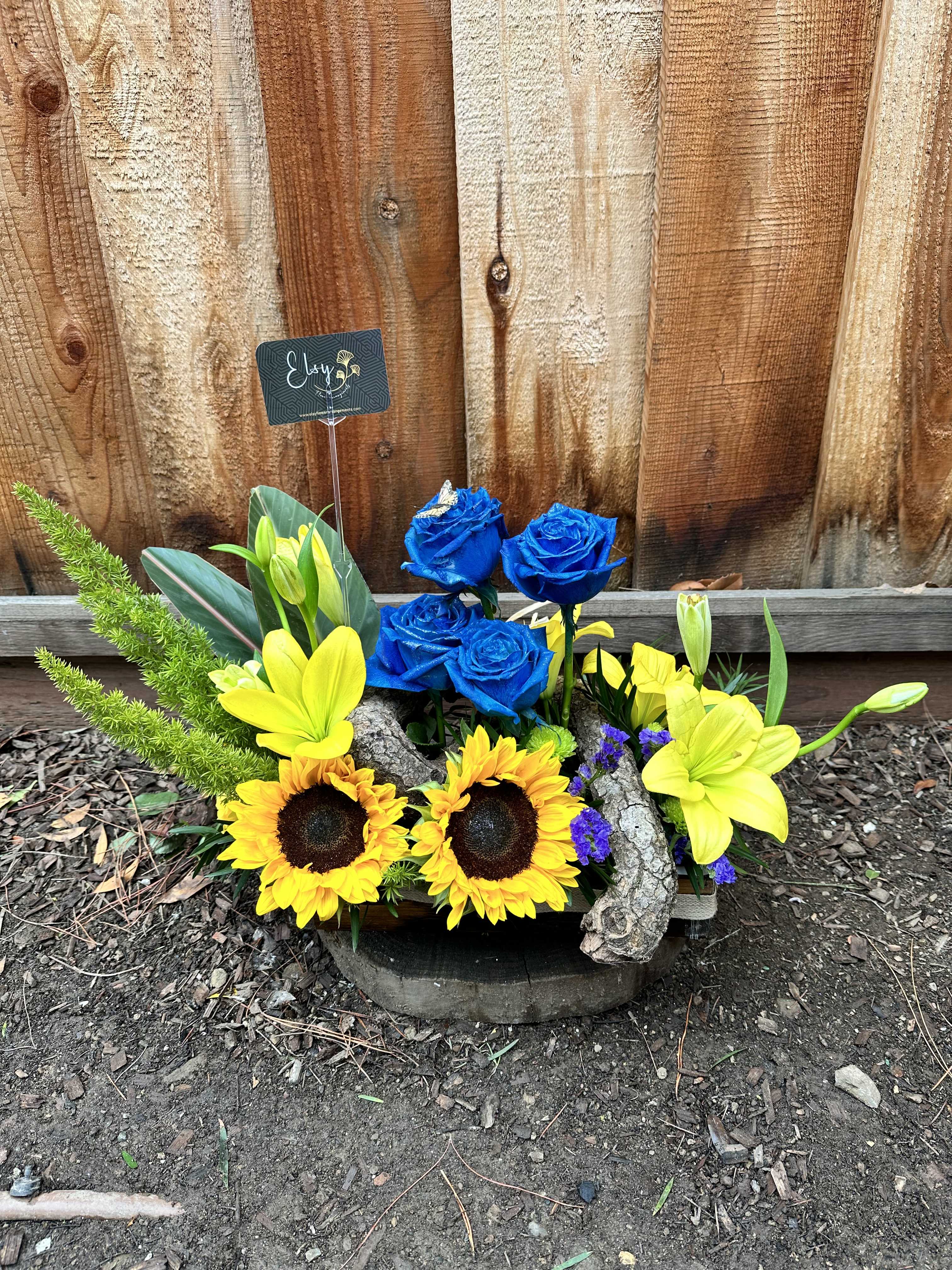 Arrangement of blue roses and yellow lilies with sunflowers in a rustic container