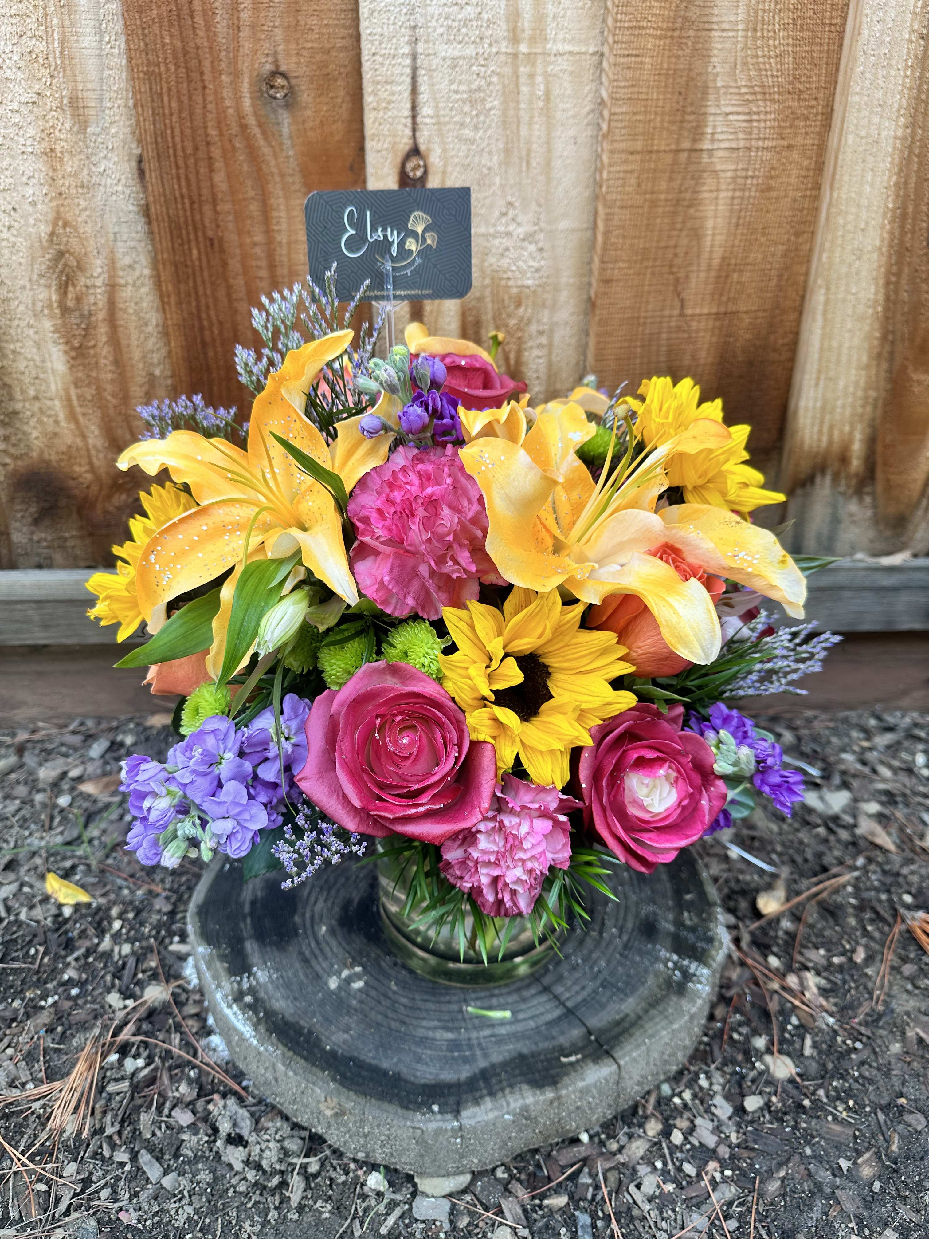 Colorful mixed bouquet in a glass vase with roses, lilies, and sunflowers