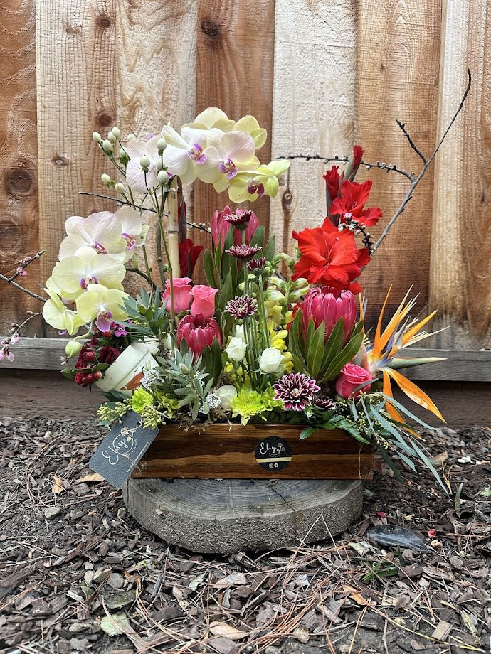 Mixed floral arrangement in a wooden box with orchids and bright tropical blooms