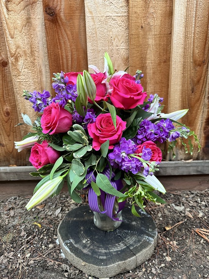 Bouquet of hot pink roses and purple flowers in a glass vase