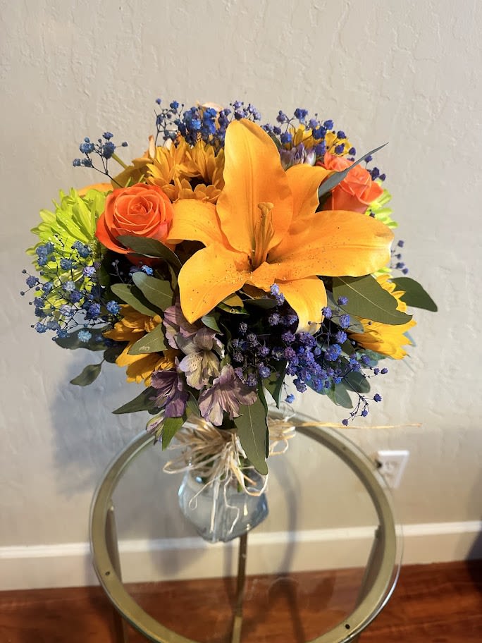 Bouquet of orange lilies, roses, and blue filler flowers in a glass vase