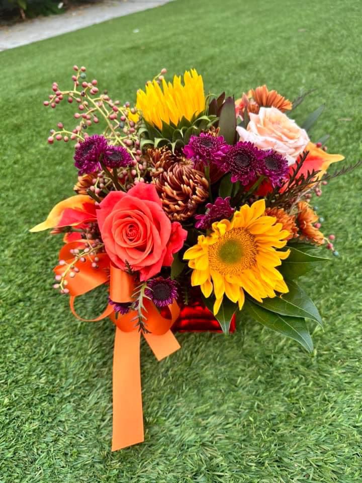 Colorful bouquet with roses, sunflowers, and purple blooms tied with orange ribbon