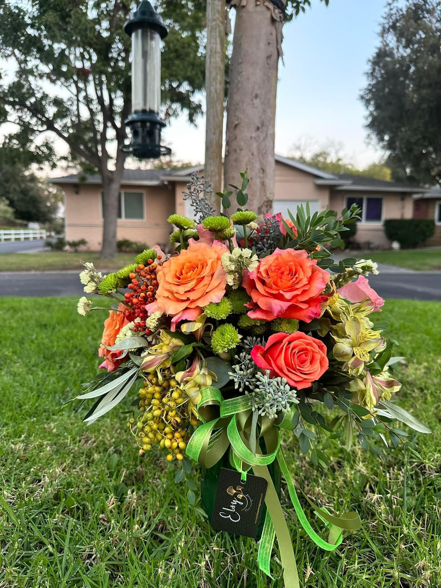 Bouquet of orange and coral roses with green accents and ribbon