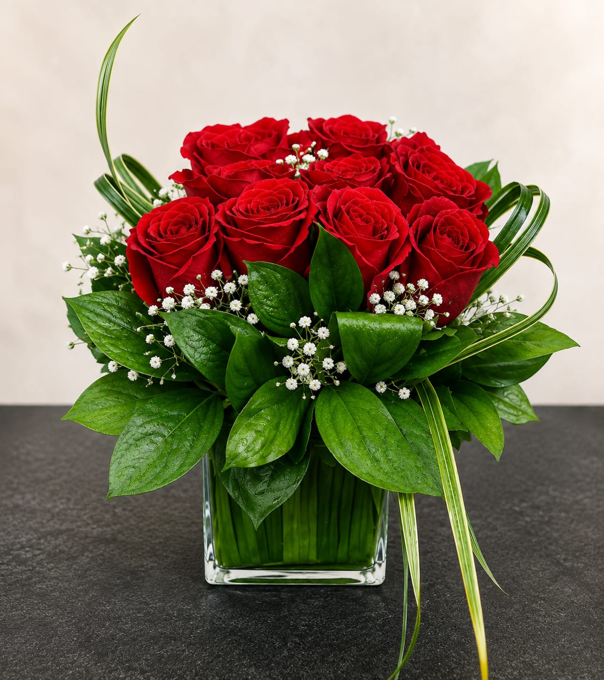 Red roses arranged in a clear square vase with white filler flowers