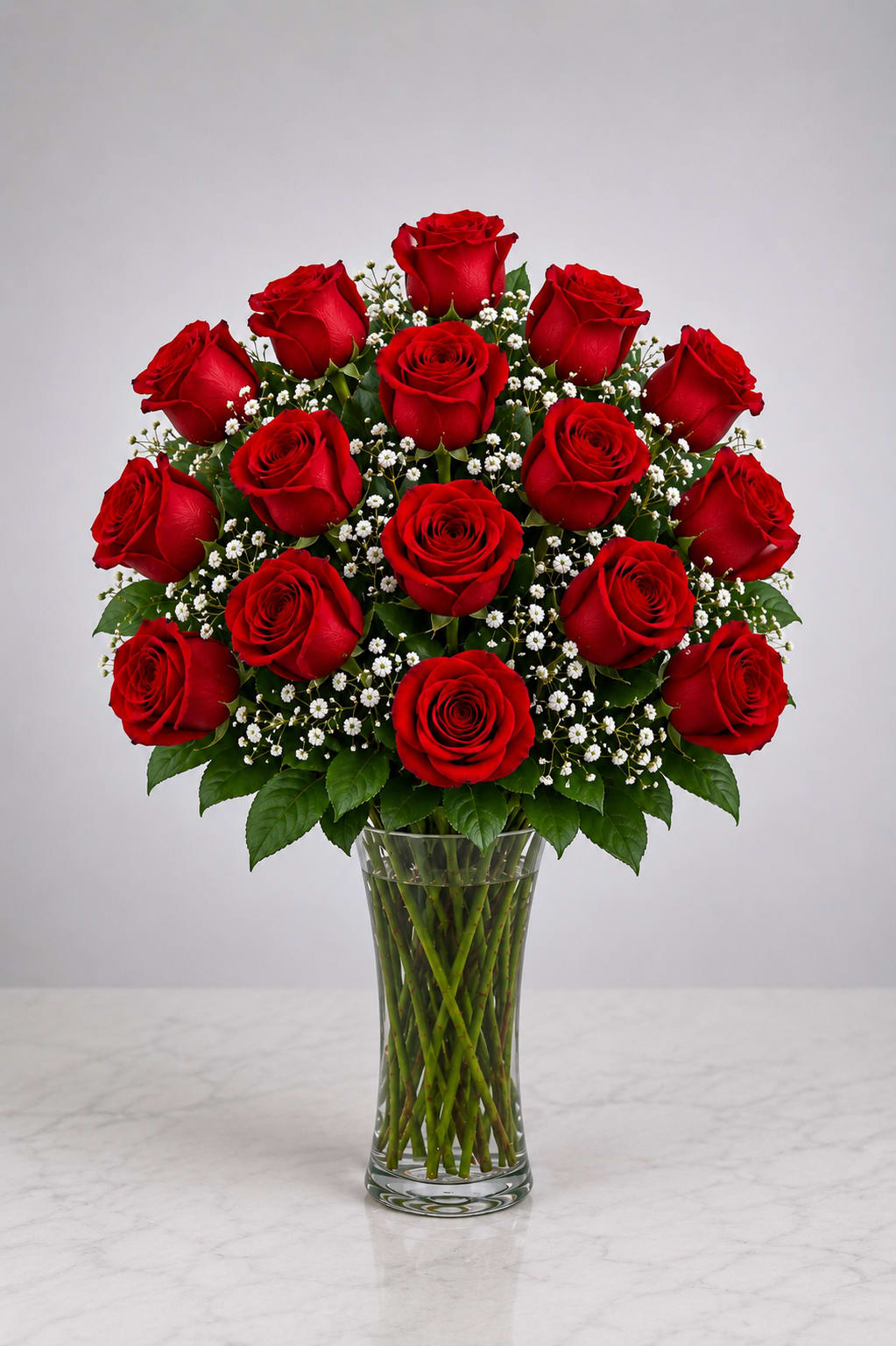 Red roses arranged in a clear glass vase with small white filler flowers