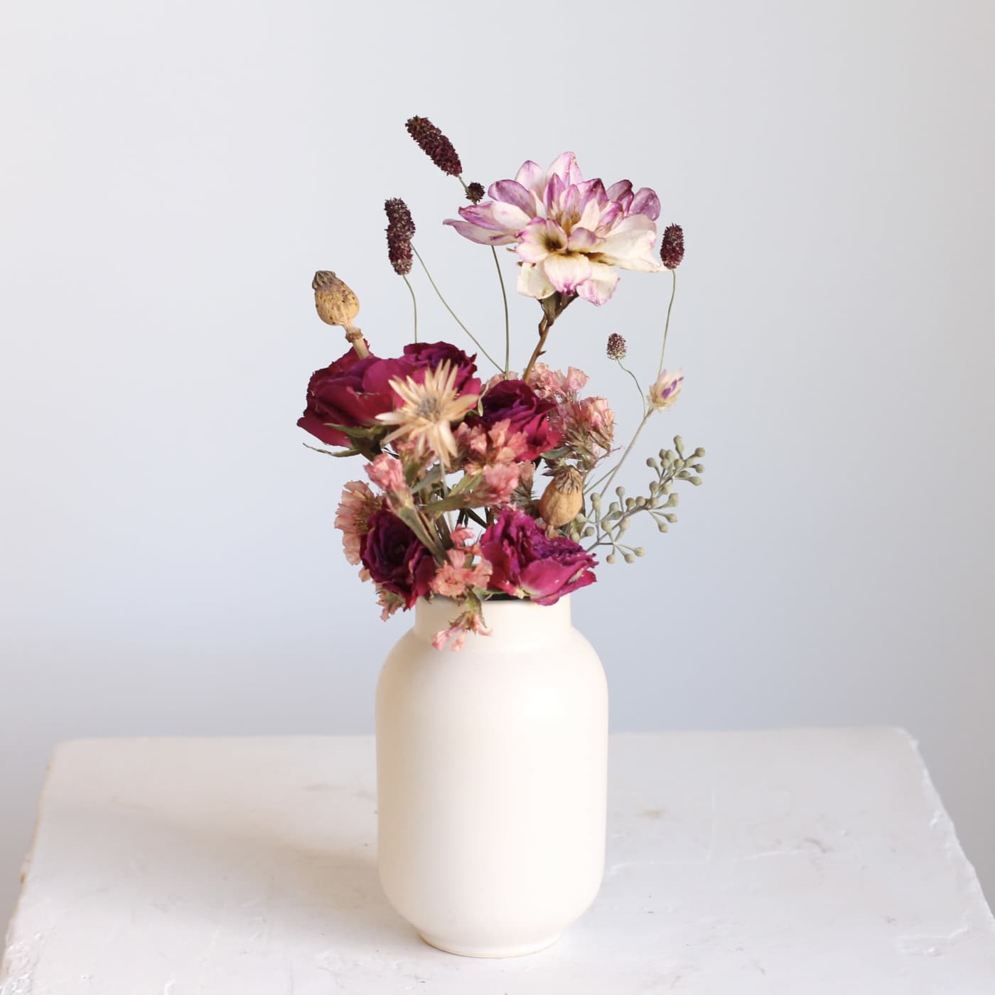 Small floral arrangement in a white vase with pink and burgundy blooms