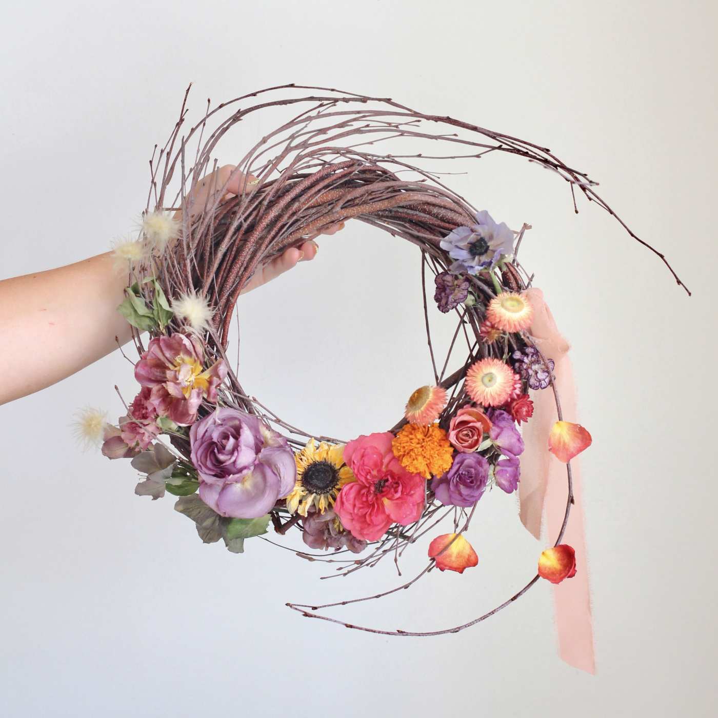 Handheld floral wreath with purple, pink, and orange blooms on a twig frame
