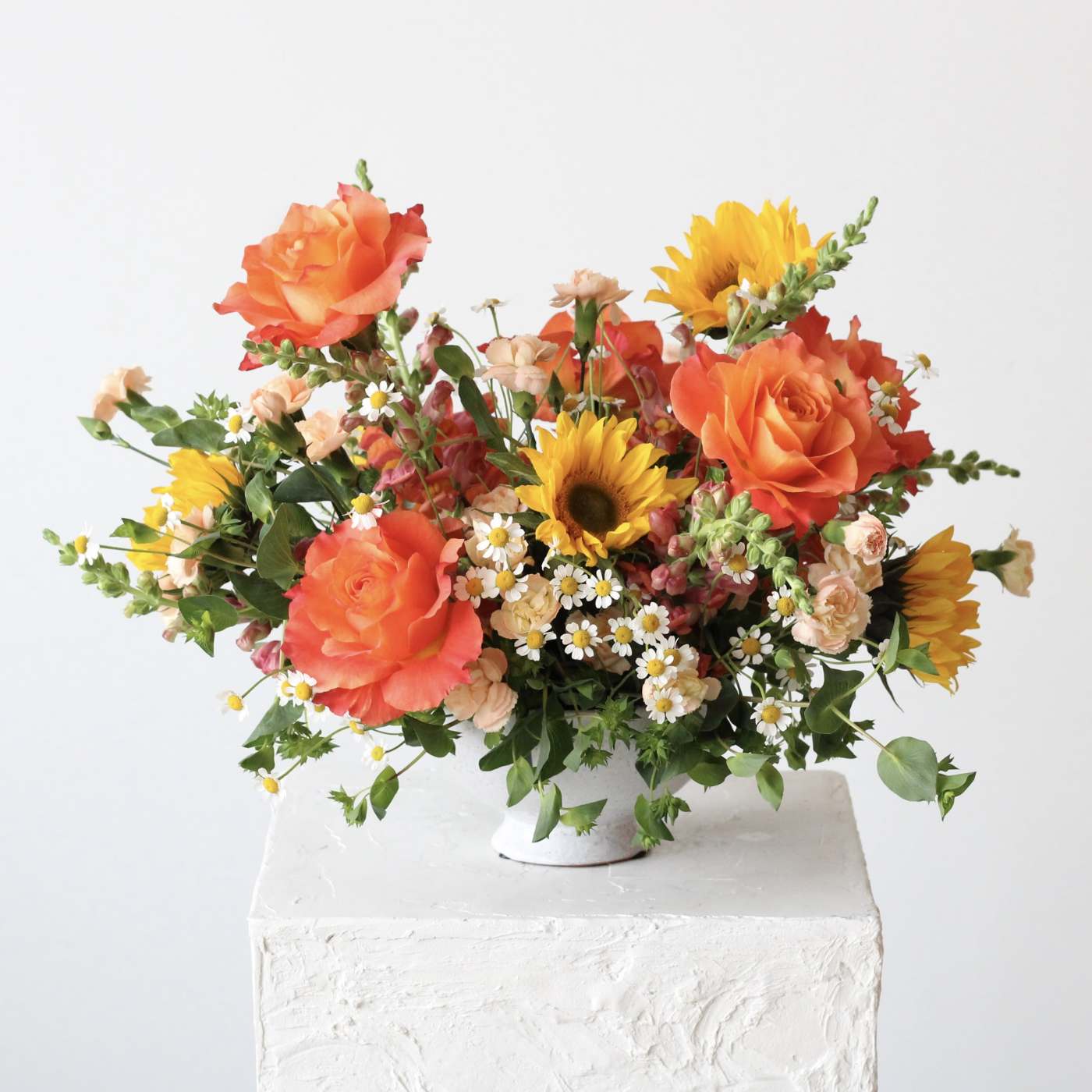 Bright mixed bouquet with orange roses and sunflowers in a white vase