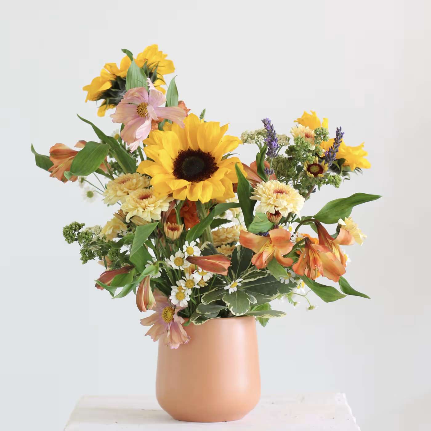 Mixed bouquet with sunflowers, orange lilies, and daisies in a peach vase