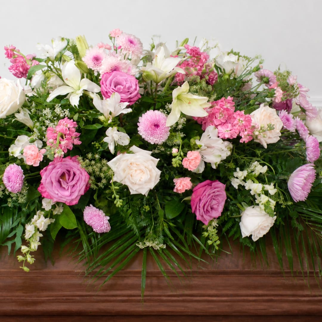 Beautiful Memory - The Beautiful Memory is a graceful casket spray filled with soft pink, blush and white blooms, thoughtfully arranged among layers of lush greenery. Roses, lilies and complementary seasonal flowers create a full garden-inspired tribute designed to honor a life remembered with love.  The pictured Deluxe design measures approximately 46 inches long. Flower varieties may vary slightly based on seasonal availability while maintaining the overall pink, blush and white color palette, style and value.