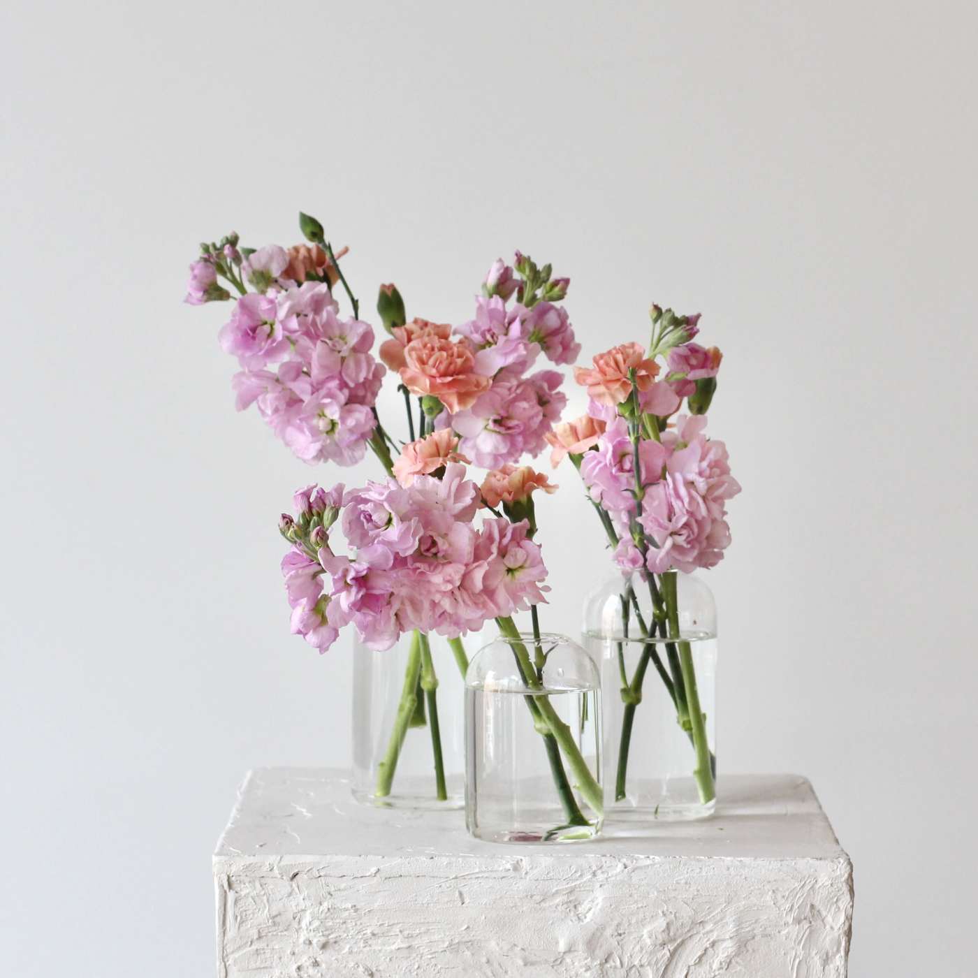 Pink and peach flowers in three clear glass vases on a white pedestal.