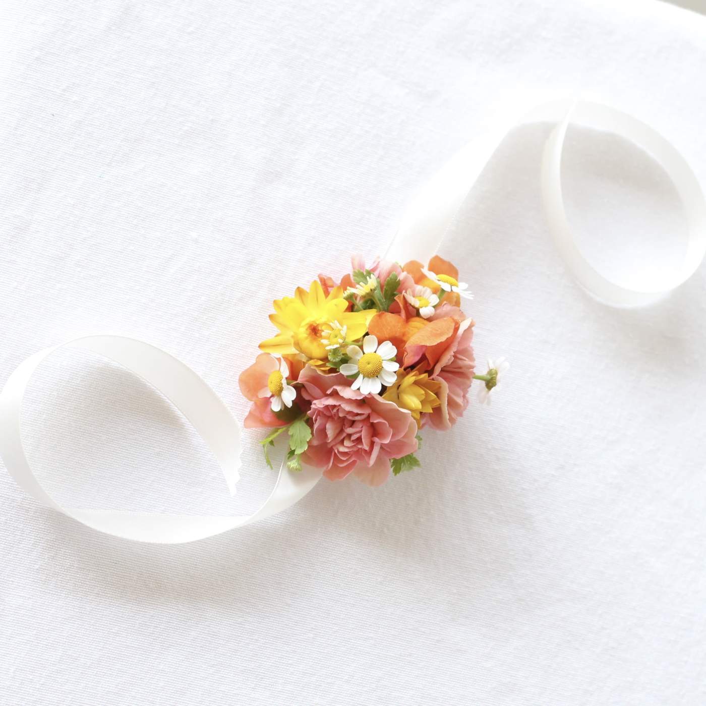 Small floral wrist corsage with pink, yellow, and orange blooms on a white ribbon