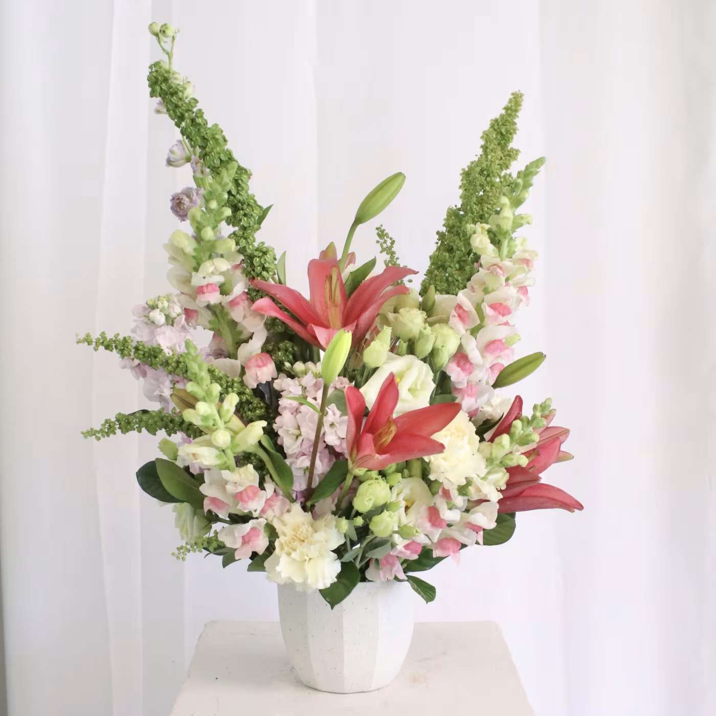 Tall mixed flower arrangement in a white vase with pink and white blooms