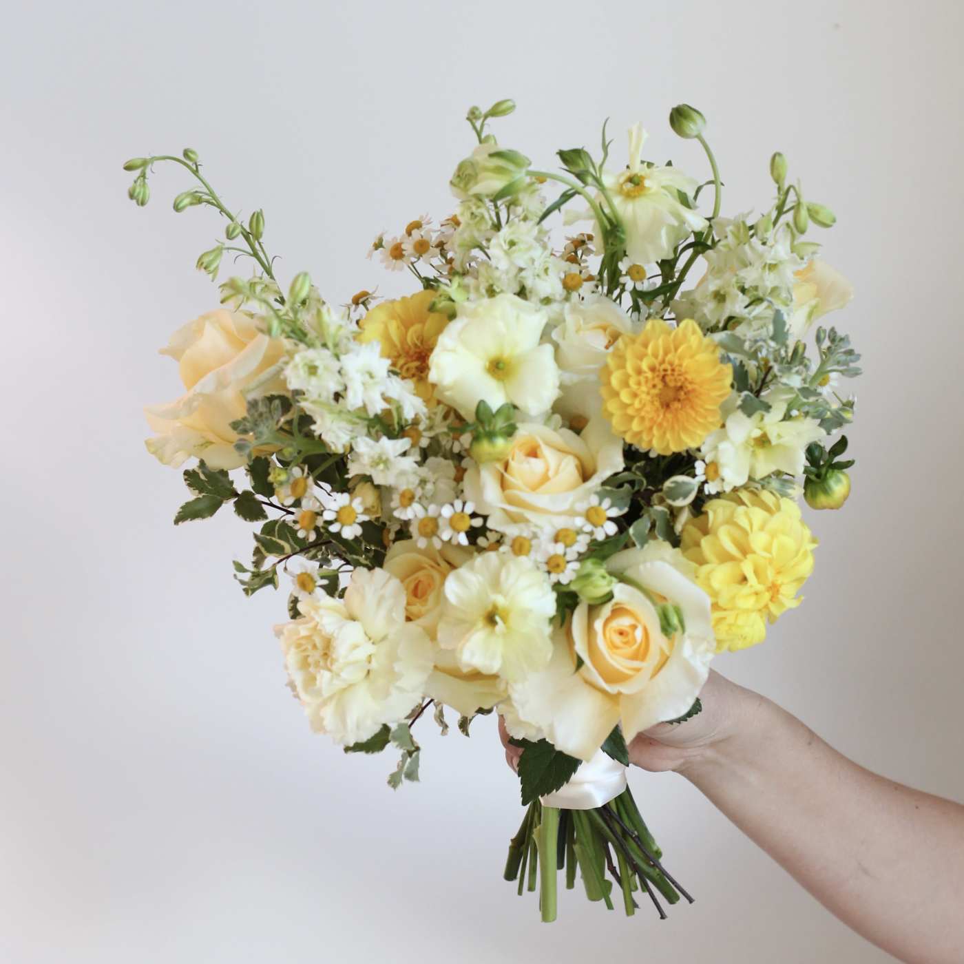Handheld bouquet of pale yellow and white flowers with small daisy accents