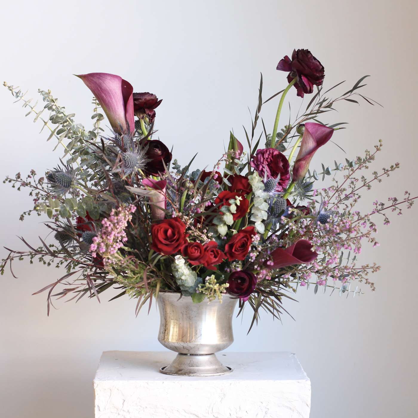 Mixed bouquet of red roses, dark calla lilies, and purple blooms in a silver vase