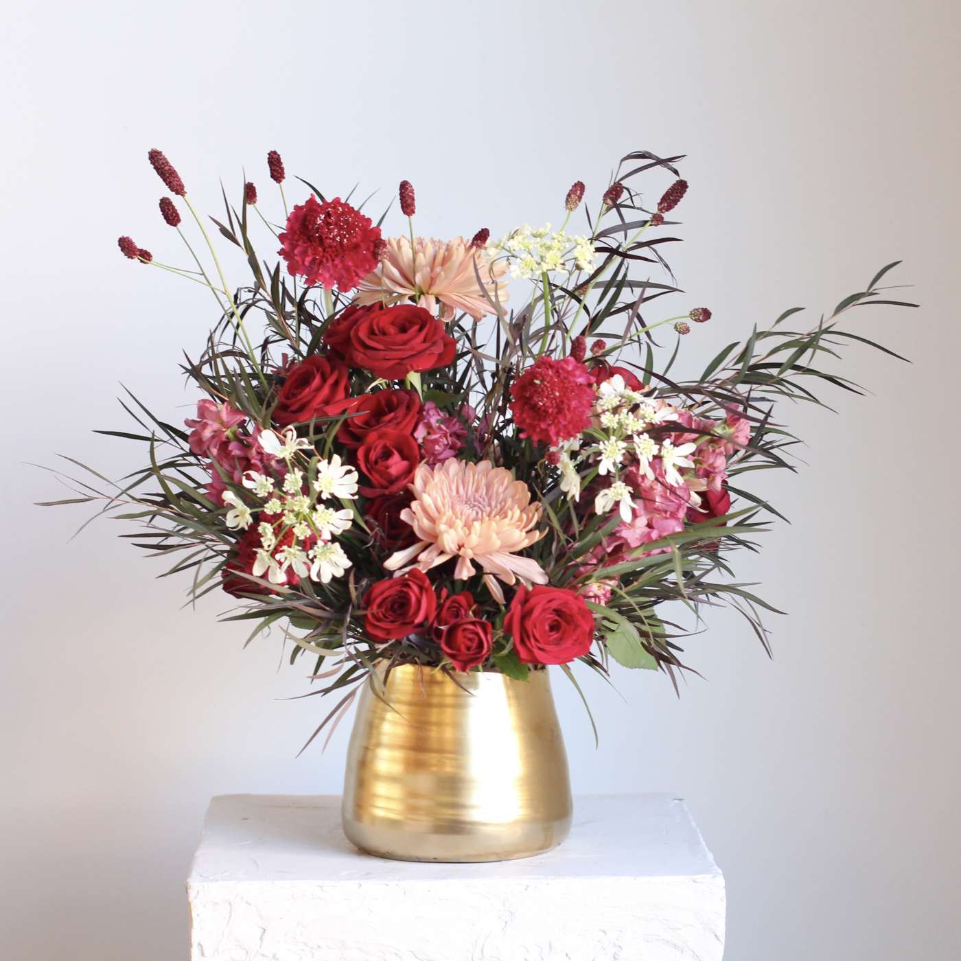 Red roses and pink blooms arranged in a gold vase