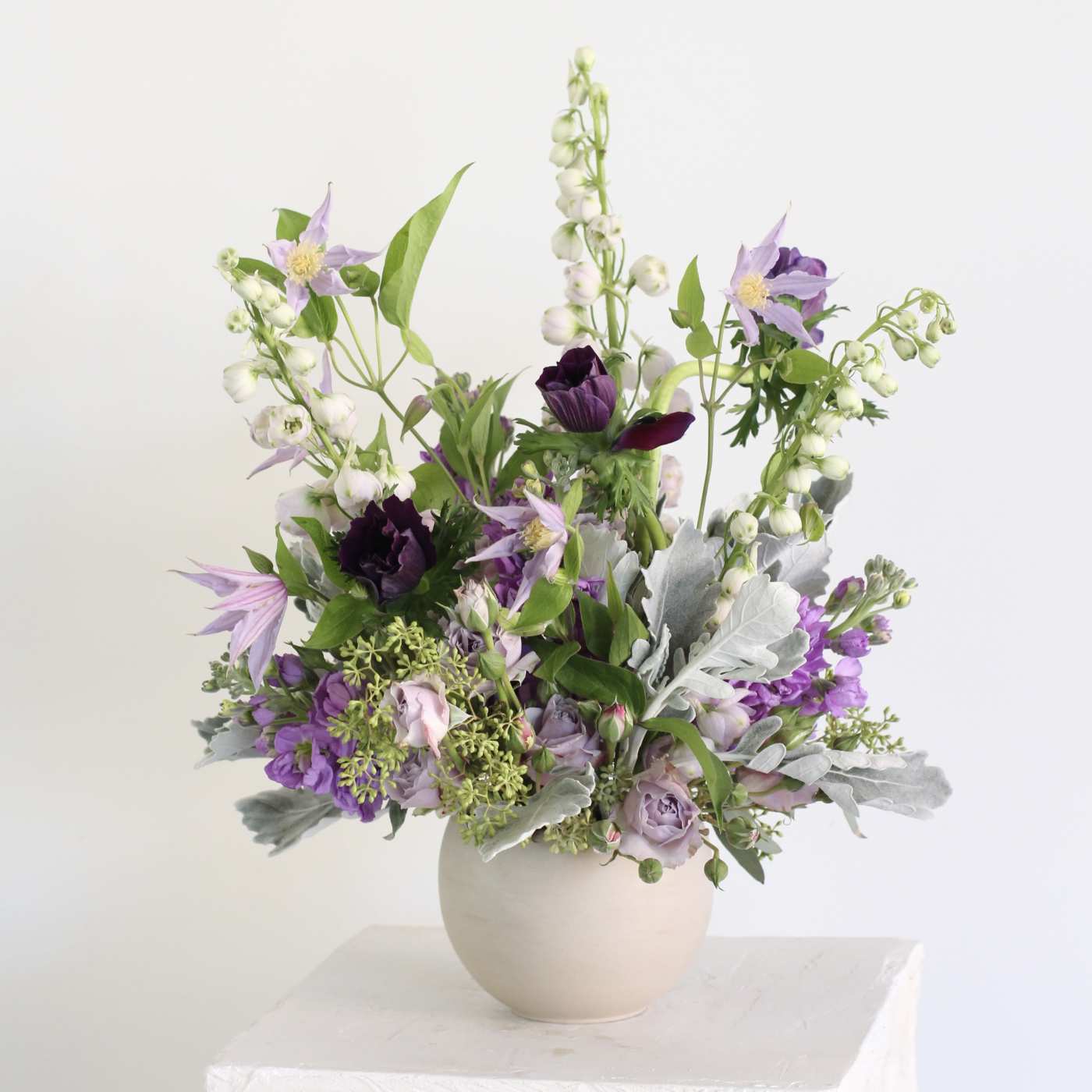 Purple and white floral arrangement in a round beige vase