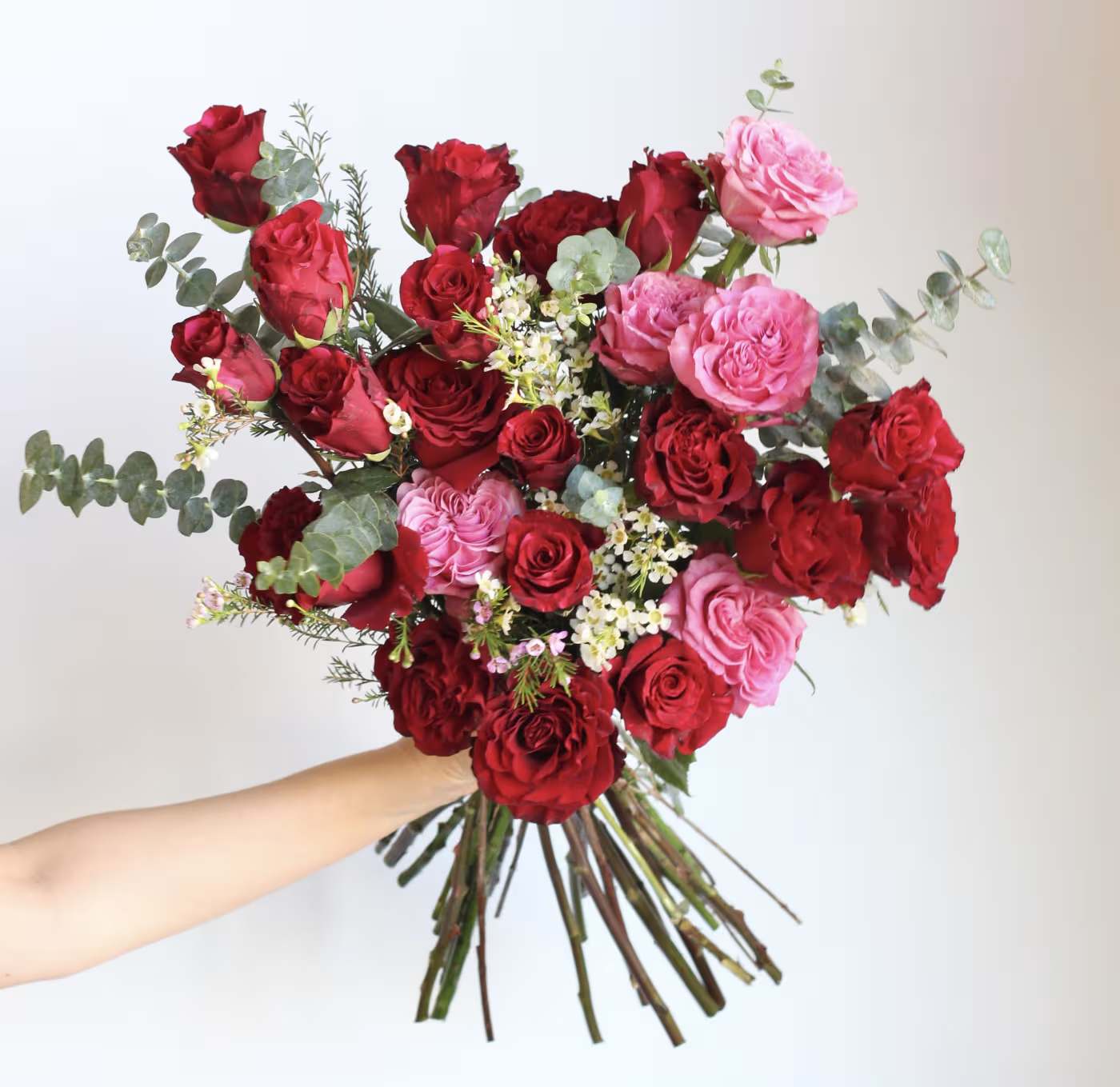 Handheld bouquet of red and pink roses with eucalyptus