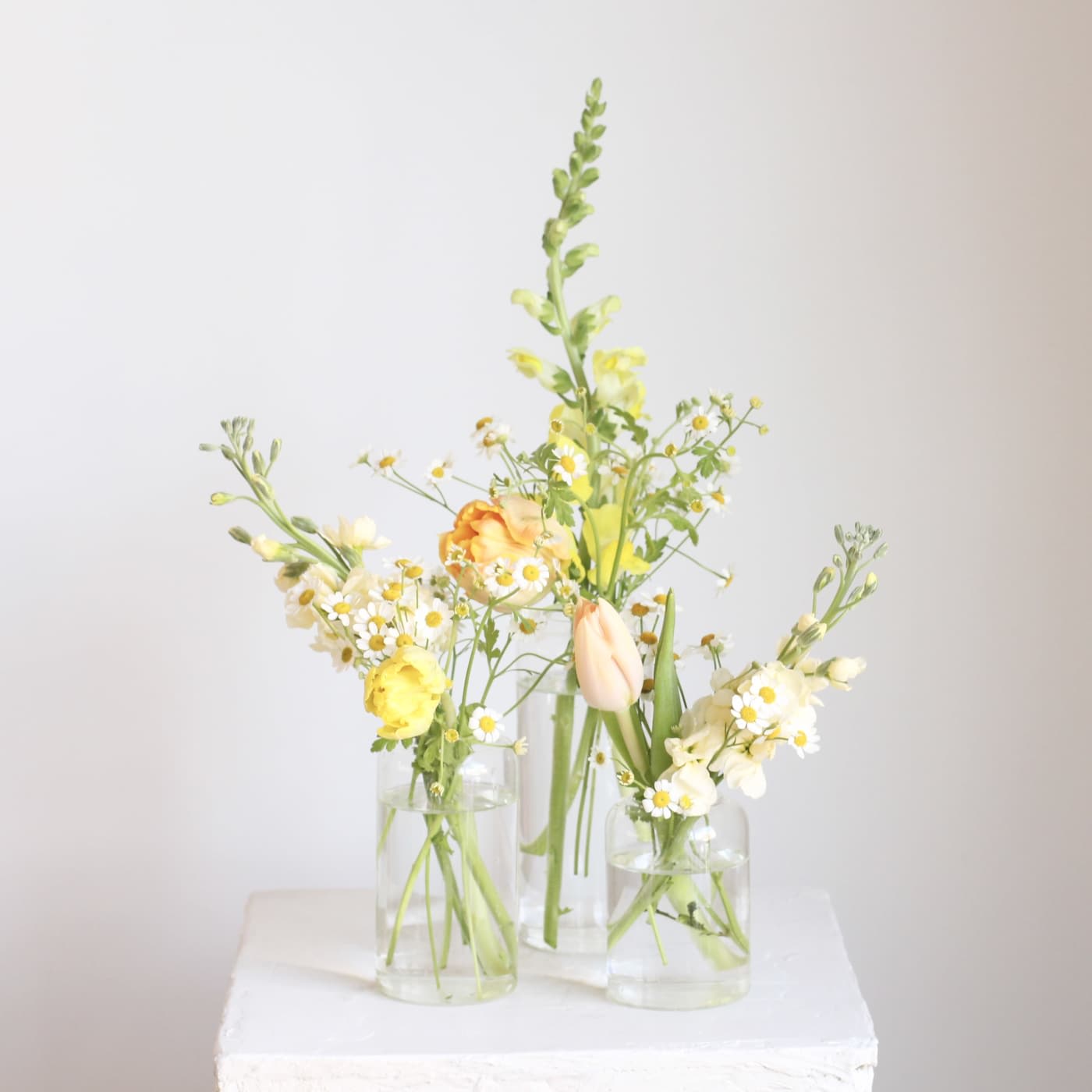 Three small glass vases hold pale yellow and white flowers.