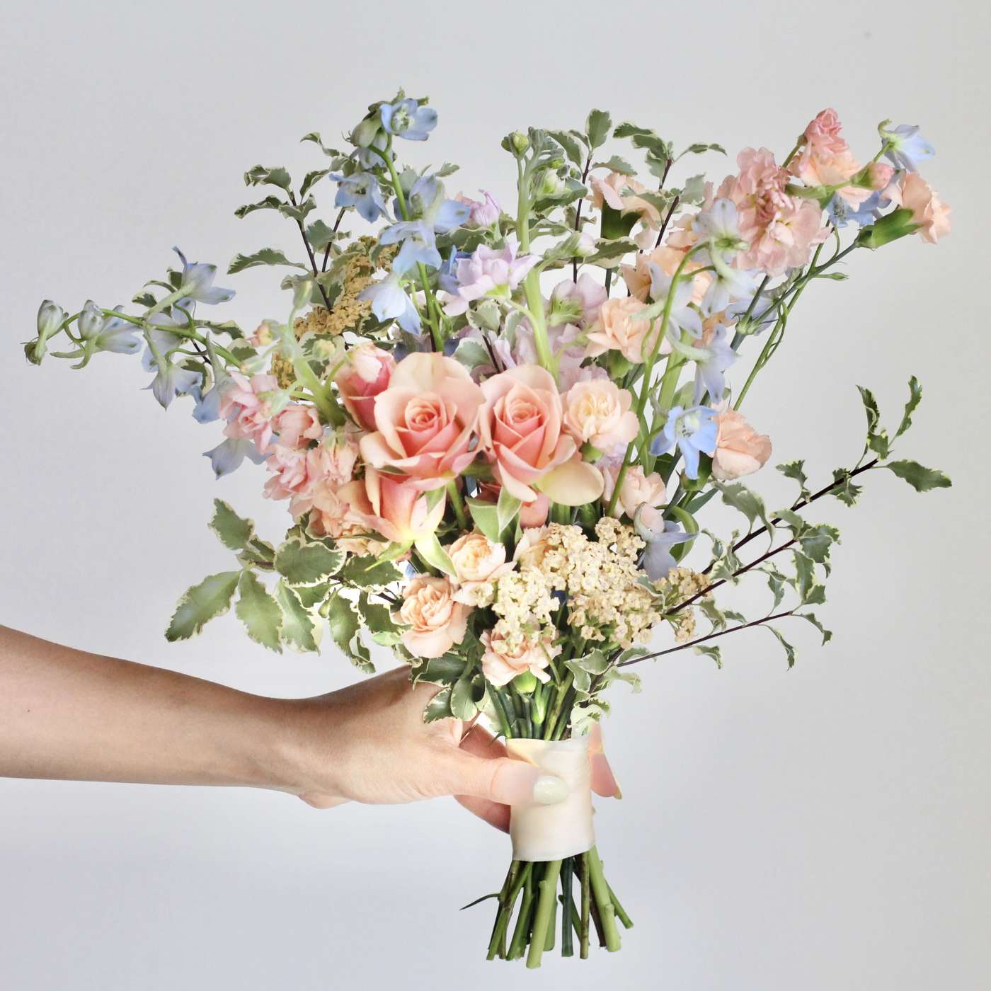 Handheld bouquet of peach roses and blue flowers