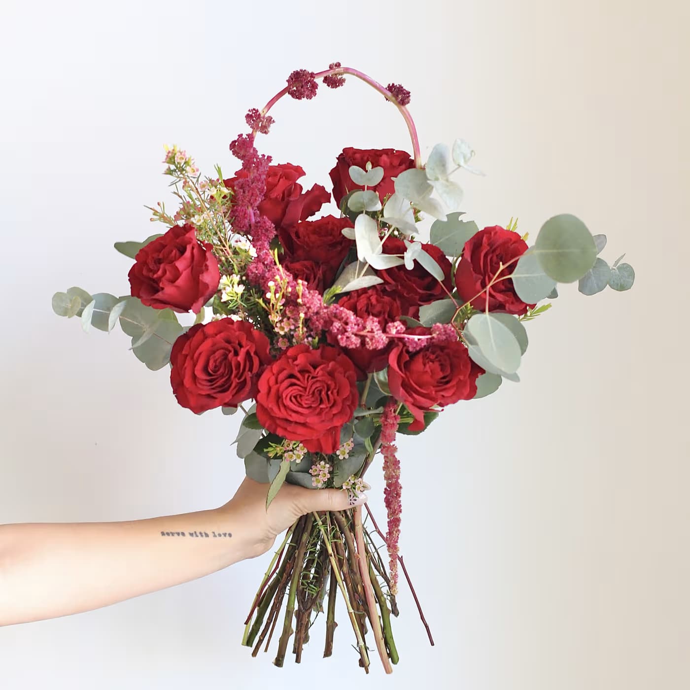 Handheld bouquet of red roses with eucalyptus and pink accents