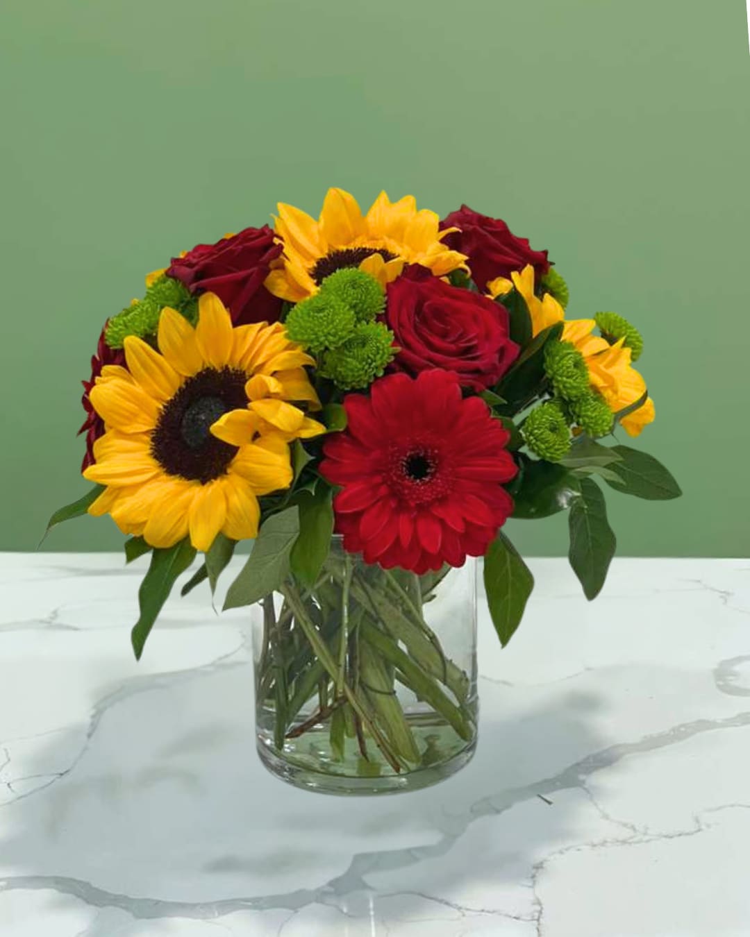 Bouquet of sunflowers, red roses, and a red gerbera daisy in a glass vase