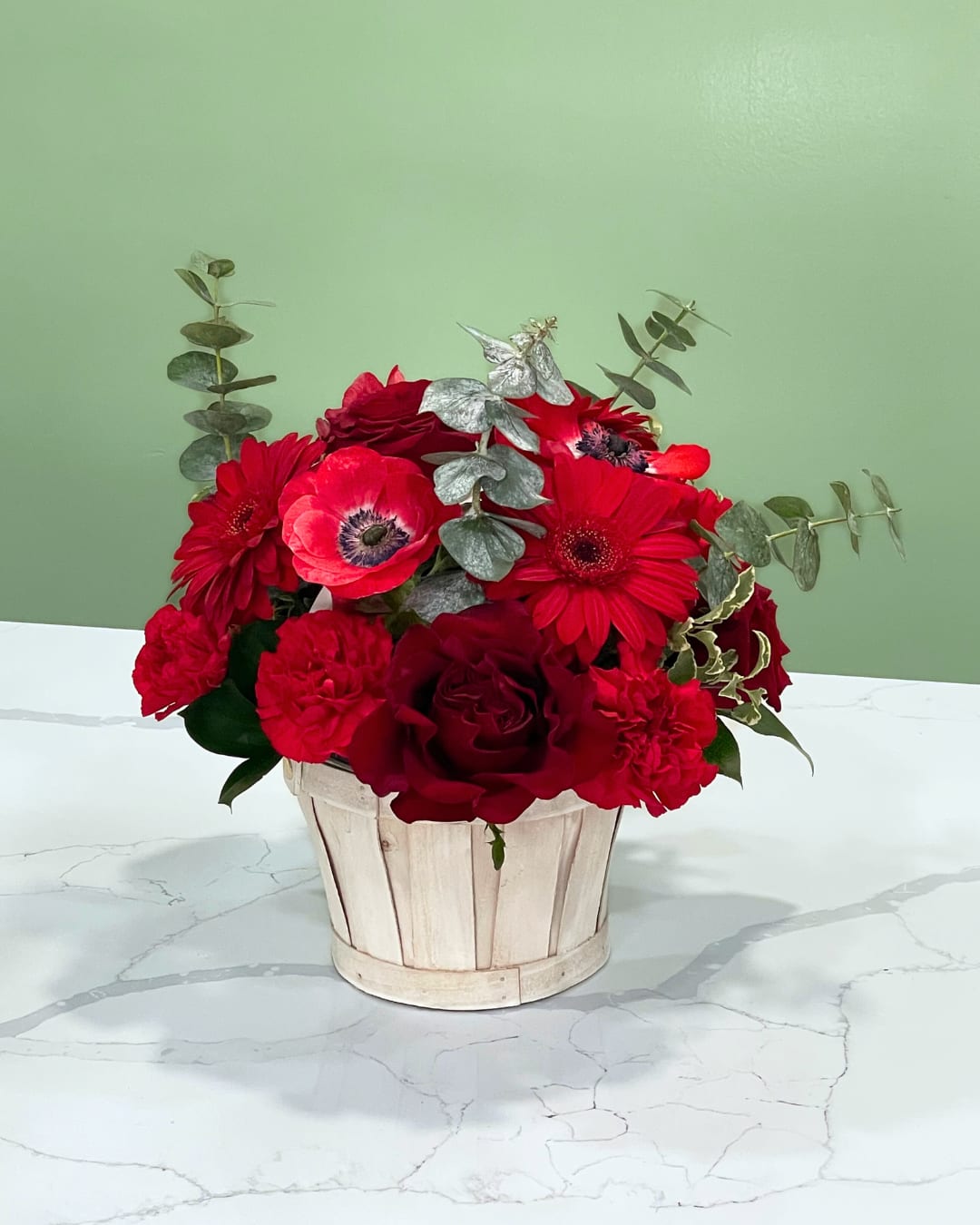 Red flowers arranged in a white wooden basket with silver eucalyptus