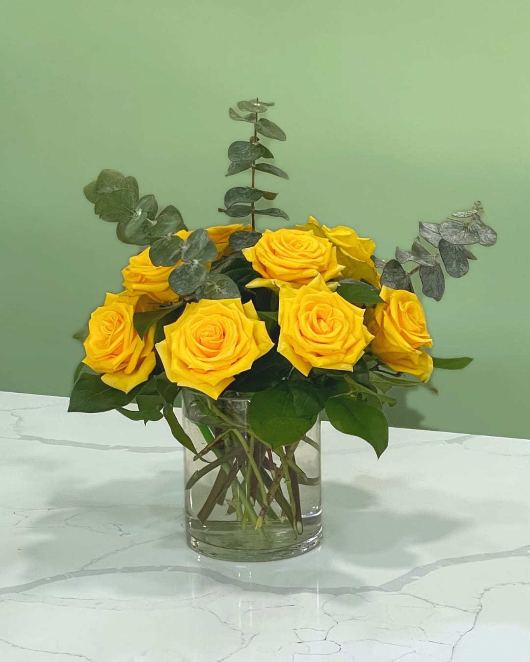 Yellow roses arranged in a clear glass vase with eucalyptus foliage