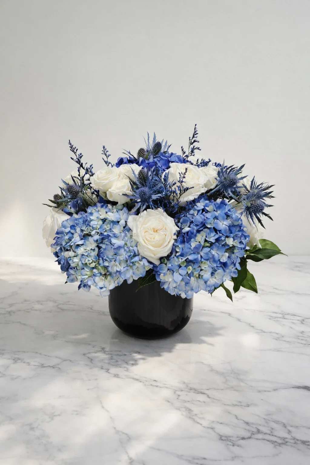 Blue hydrangeas and white roses arranged in a black vase