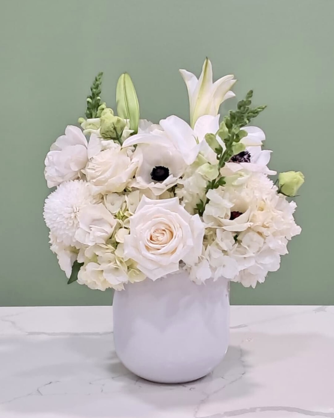 White floral arrangement in a white vase with lilies and roses