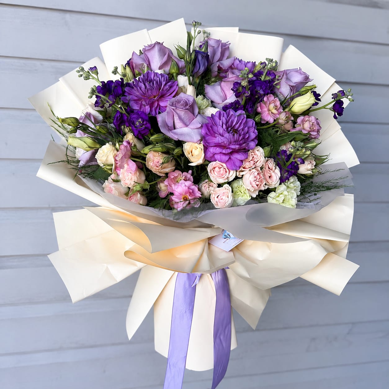 Bouquet of purple and pink flowers wrapped in cream paper with a lavender ribbon