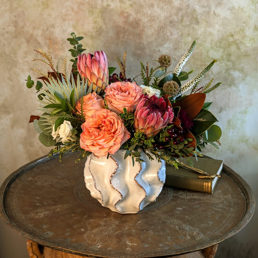 Peach roses and protea in a white ceramic vase