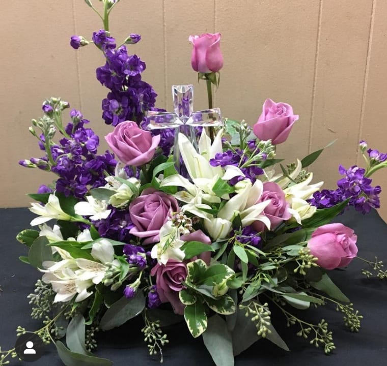 Purple and pink roses with white lilies around a clear cross