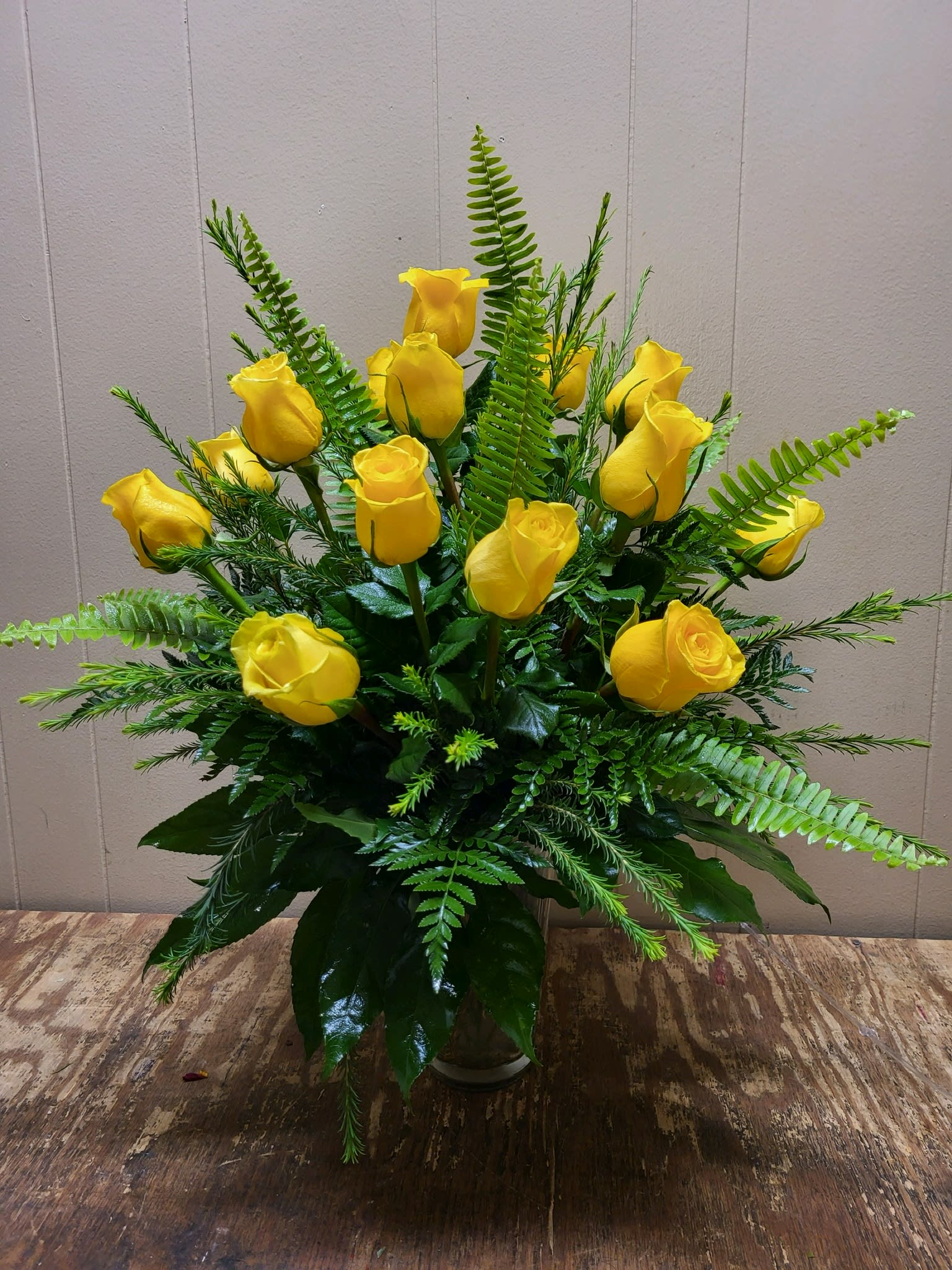 Yellow roses arranged in a glass vase with fern foliage
