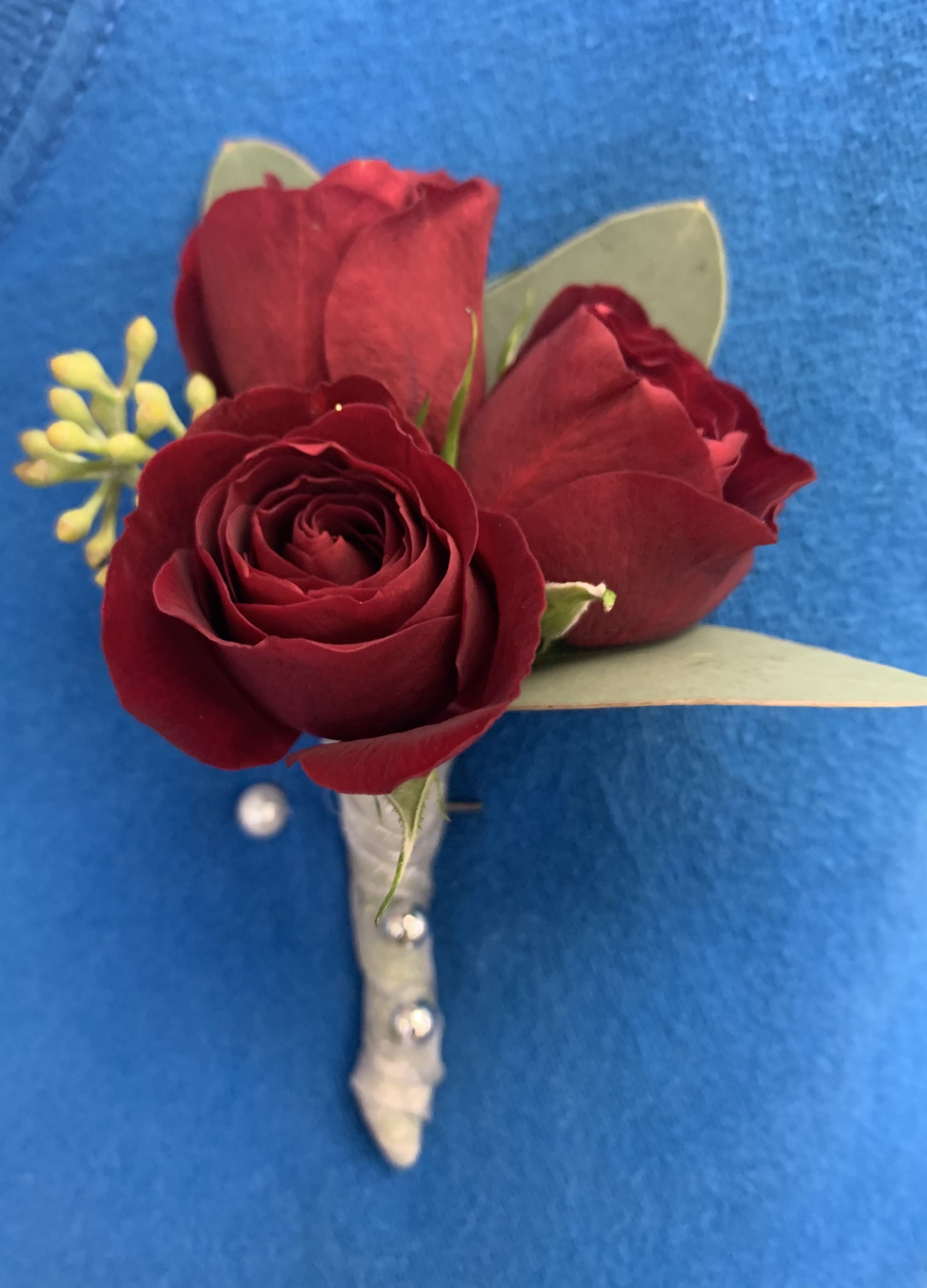 Red Celebration Boutonniere - This boutonniere is available in red, white, pink, orange and yellow- please note color if roses and ribbon in special instructions, if nothing is listed we will make as pictured…  3 Red Small Sweetheart roses and seeded eucalyptus.  Wrapped in silver ribbon, perfect for a black tie event.