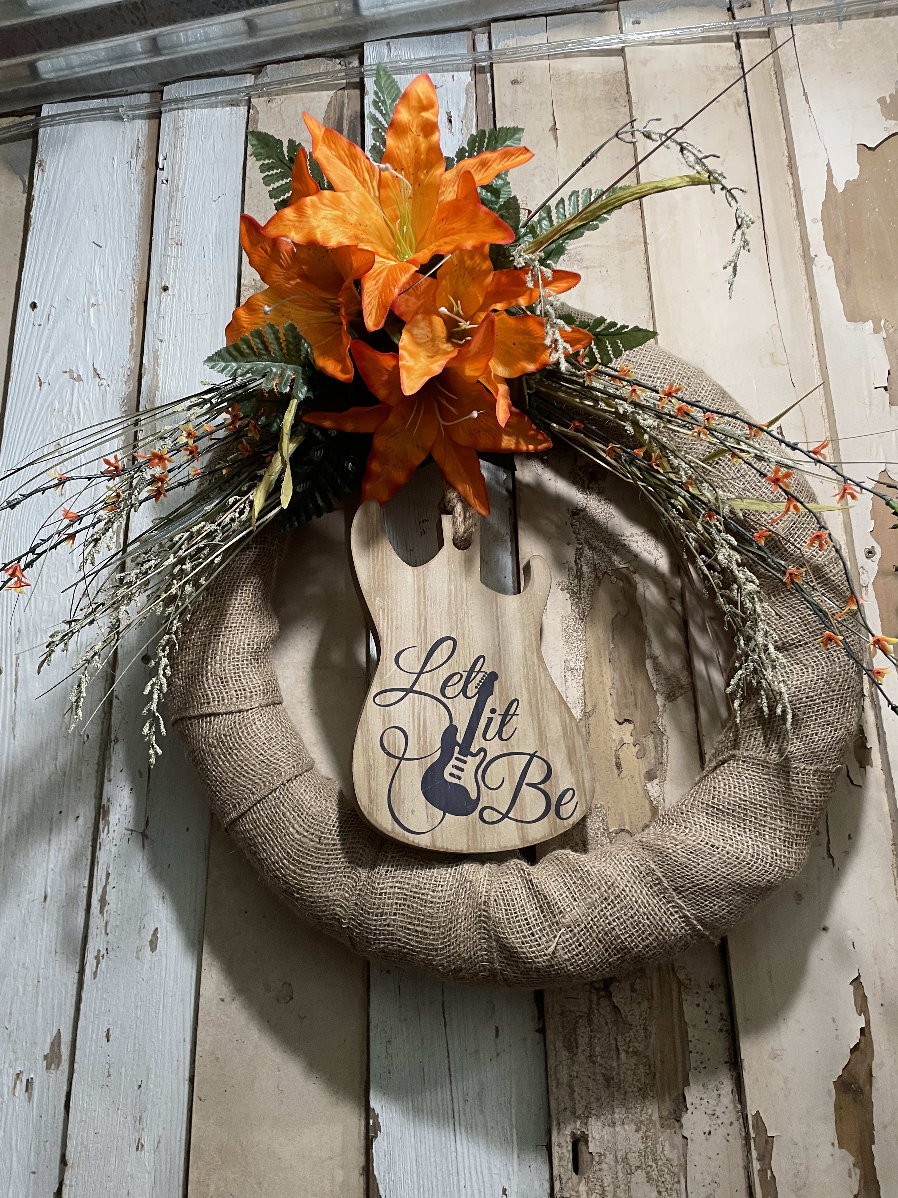 Orange lilies on a burlap wreath with a wooden guitar sign