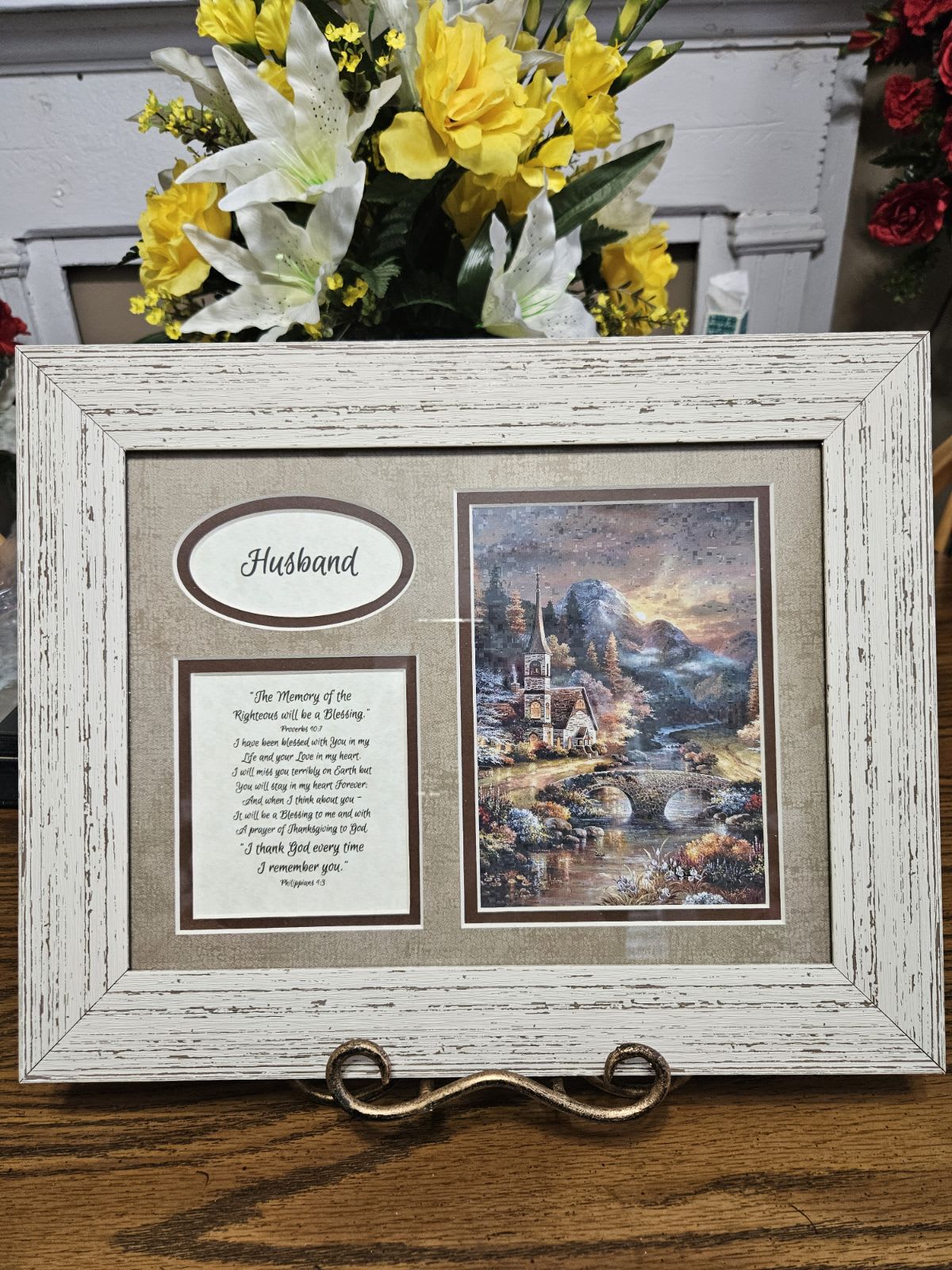 Framed memorial display with yellow and white flowers behind it