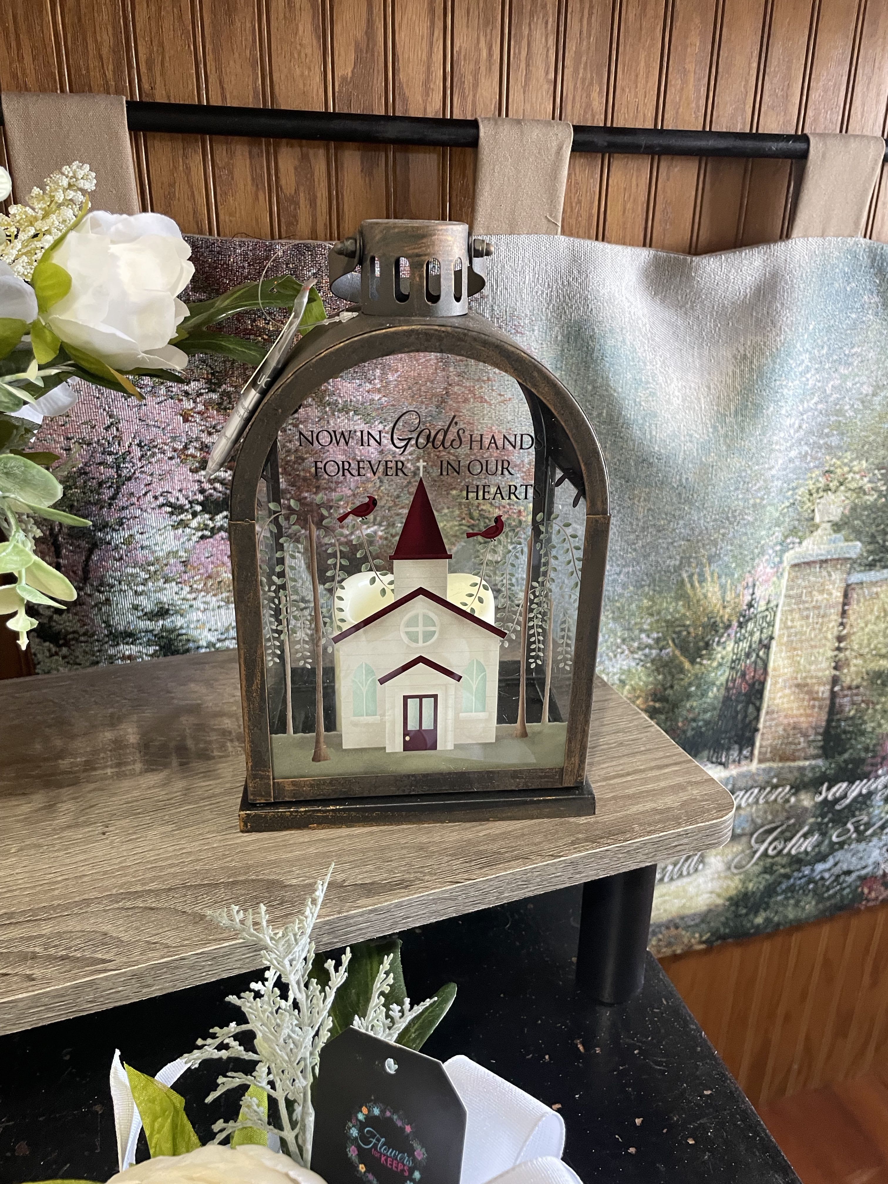 Memorial lantern with a church scene and white flowers beside it