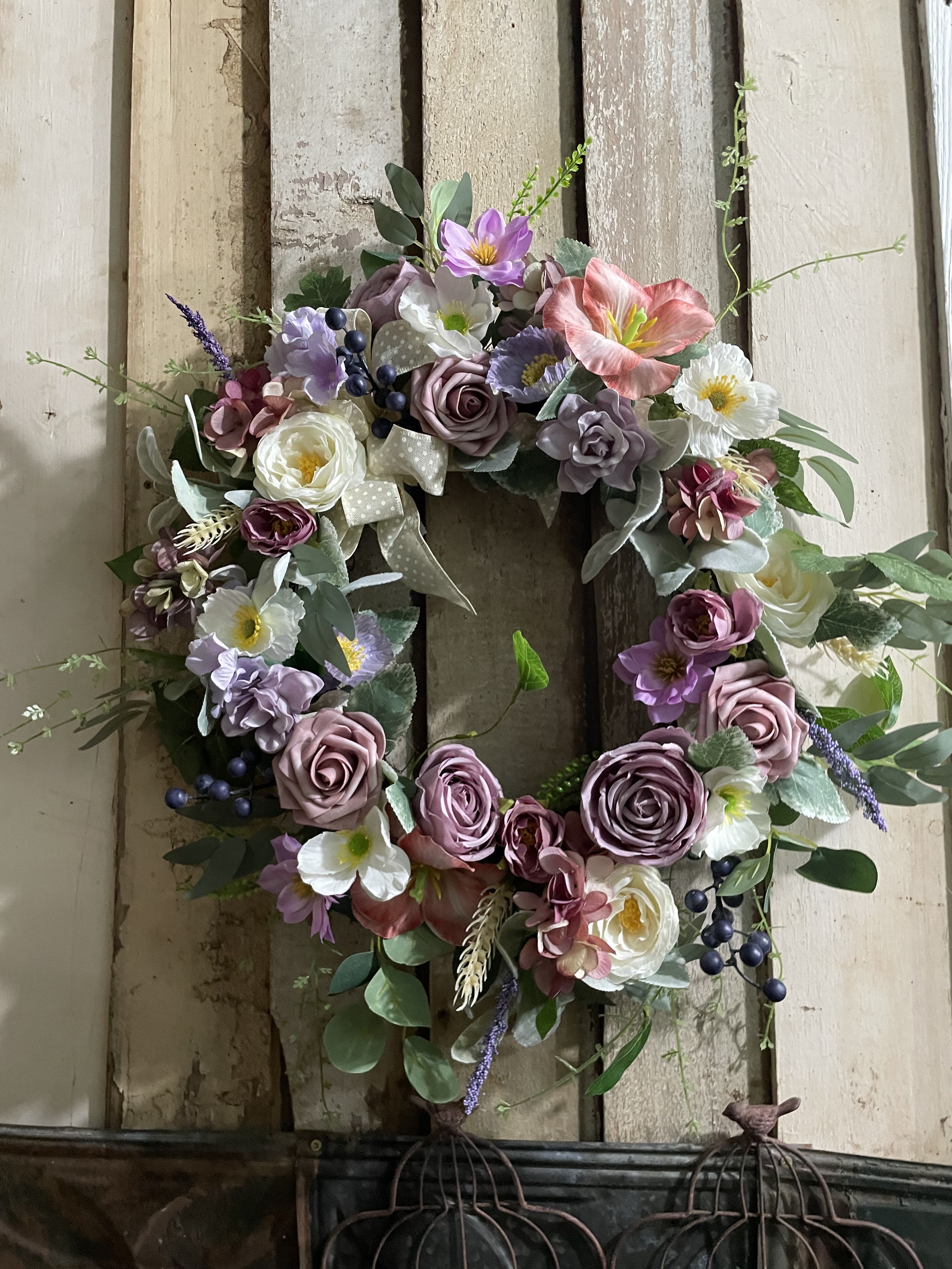 Floral wreath with pink, purple, and white blooms on a rustic wood background