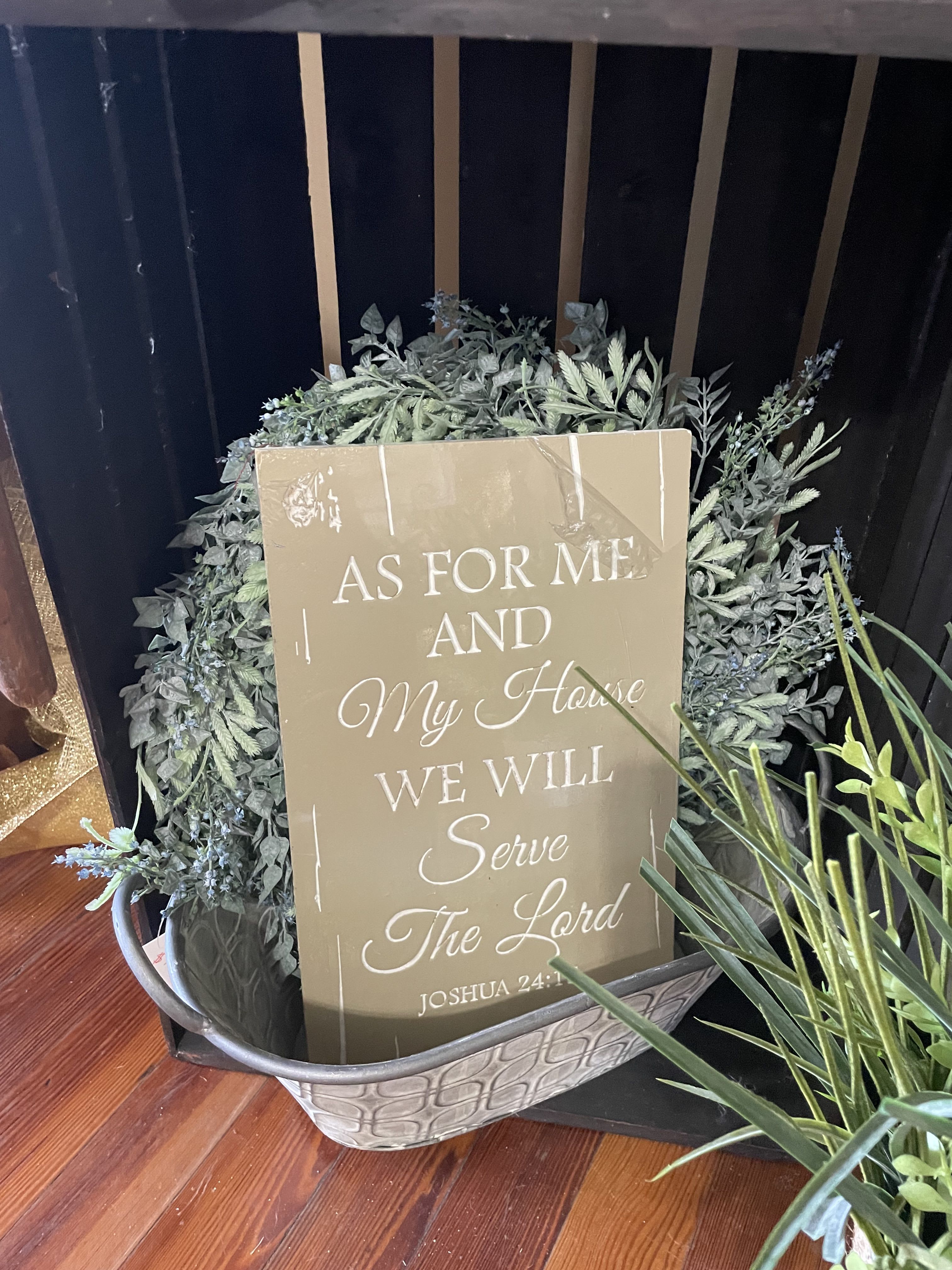 Decorative greenery arrangement in a metal basket with a scripture sign