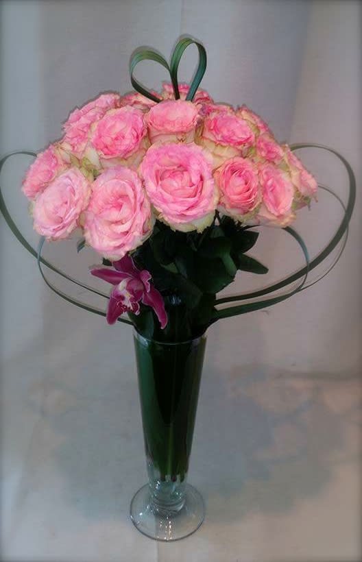 Pink roses arranged in a tall glass vase with decorative loops