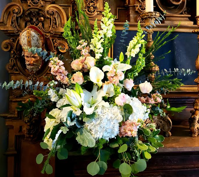 Large white floral arrangement with lilies, calla lilies, and pastel blooms
