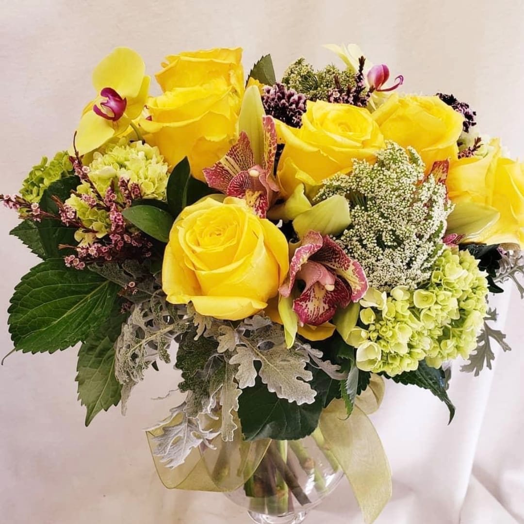 Yellow roses and orchids arranged in a clear glass vase