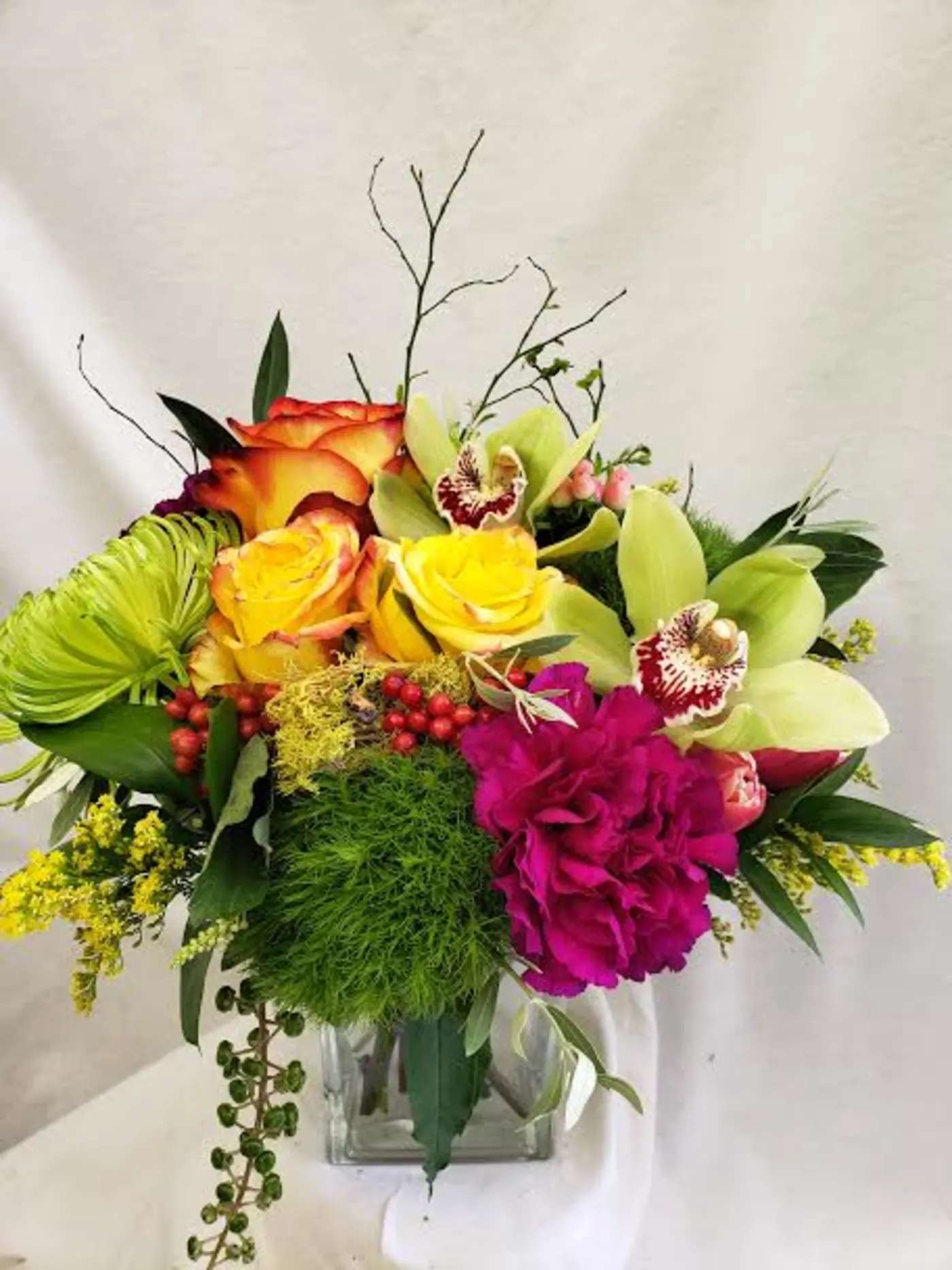 Colorful bouquet with roses, orchids, and a glass vase